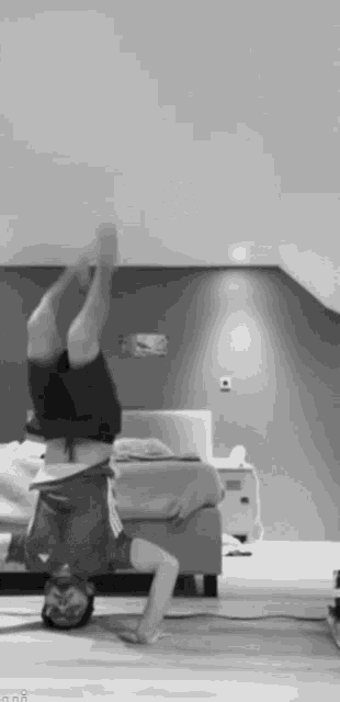 a black and white photo of a person doing a handstand in a bedroom .