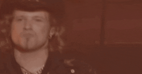 a man wearing a hat and a leather jacket is looking at the camera in a black and white photo .