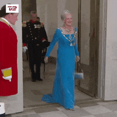 a woman in a blue dress is walking into a room with a man in a red coat and a tv2 logo on the door