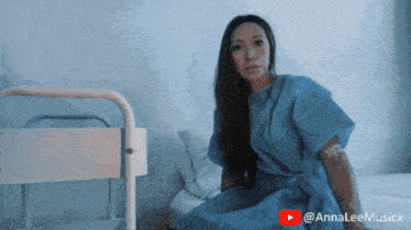 a woman in a hospital gown is sitting on a bed with a youtube play button behind her