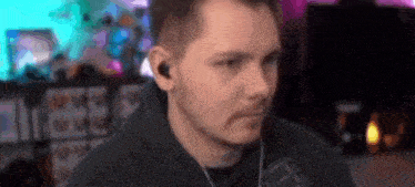 a man wearing headphones is sitting in front of a fireplace and looking at the camera .