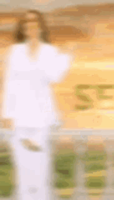 a blurry picture of a woman in a white shirt and white pants standing in front of a building .