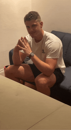 a man wearing a watch sits on a couch with his hands together