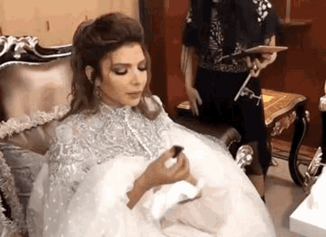 a woman in a white dress is sitting on a couch holding a bottle of lipstick .