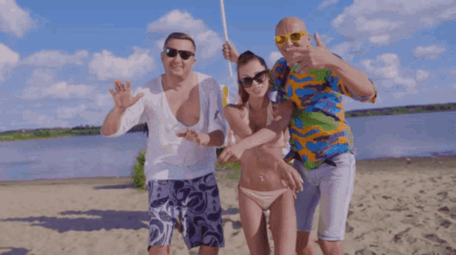 two men and a woman are posing for a picture on a sandy beach