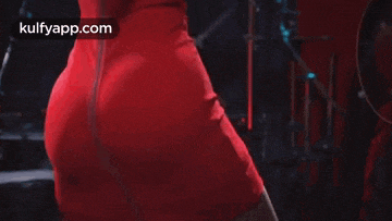 a woman in a red dress is dancing on a stage in front of drums .