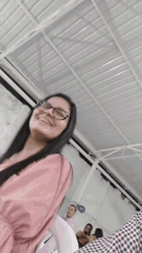 a woman wearing glasses and a pink shirt is smiling in a room