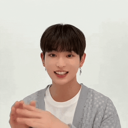 a young man wearing a grey cardigan and a white t-shirt is waving his hands .