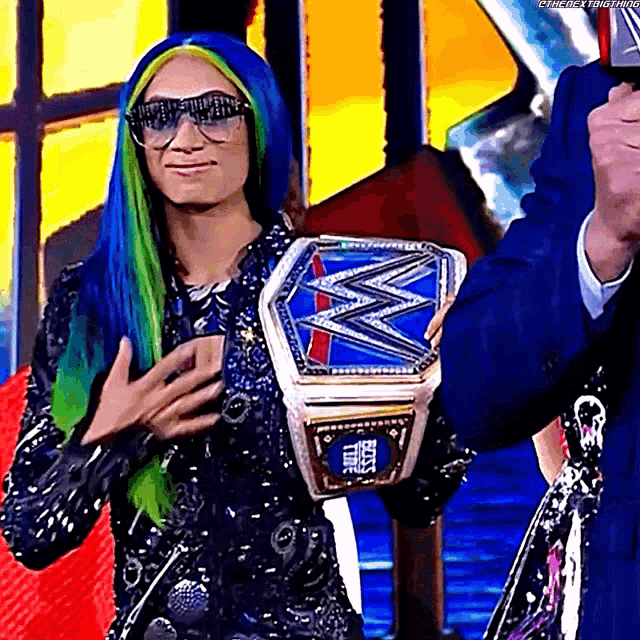 a woman with blue and green hair is holding a wrestling championship .