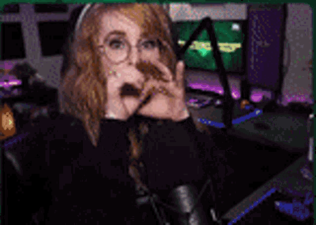 a woman wearing glasses is sitting in front of a microphone and covering her mouth .