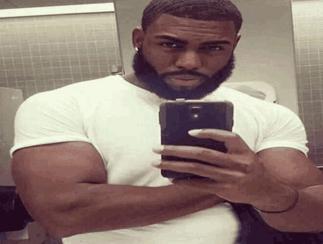 a man with a beard is taking a selfie in a public restroom