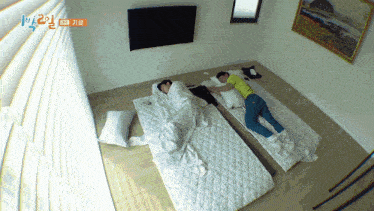 two people laying on mattresses in a room with a tv and a painting