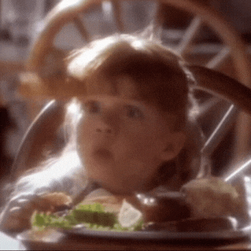 a little girl is sitting at a table with a plate of food