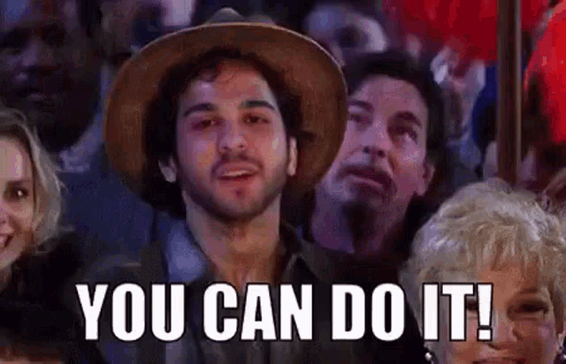 a man in a hat is sitting in a crowd of people and saying `` you can do it ! ''