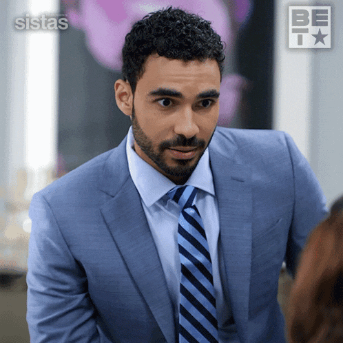 a man in a suit and tie is standing in front of a sign that says " sistas "