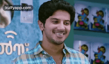 a man in a plaid shirt is smiling while standing in front of a bookshelf .
