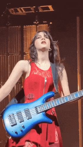 a woman in a red dress plays a blue bass guitar