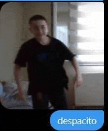 a man in a black shirt is standing in front of a window in a bedroom .