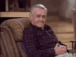 an older man is sitting in a chair with his hands folded and smiling .