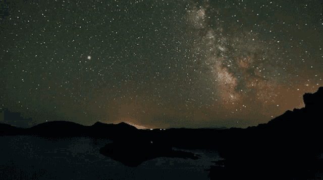 the milky way is visible in the night sky over a lake