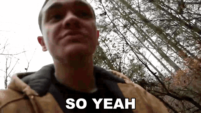 a man in a brown jacket is standing in the woods and saying so yeah