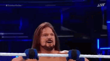 a man without a shirt is sitting in a wrestling ring with his hands on a bar .