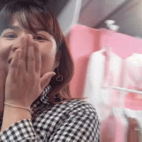 a woman in a plaid shirt and heart shaped earrings is covering her mouth with her hands .