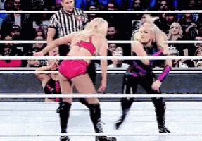 two women are wrestling in a ring with a referee watching .