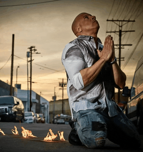 a man is kneeling down with his hands folded in front of a fire