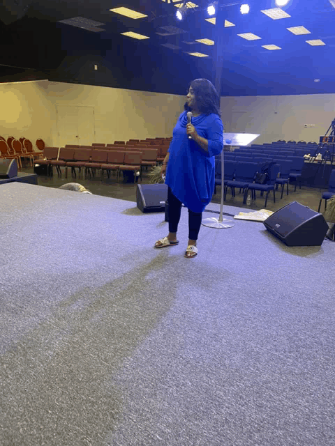 a woman in a blue shirt is standing on a stage holding a microphone