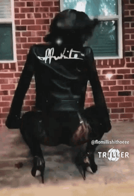 a woman wearing a black leather jacket and high heels is squatting in front of a brick wall ..