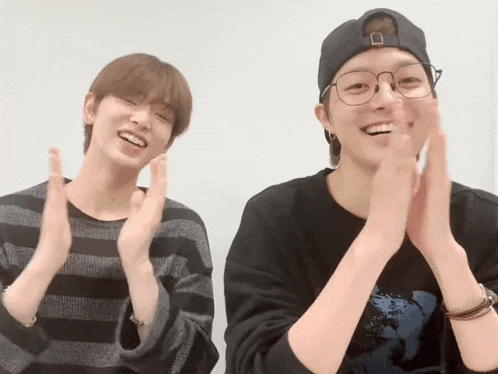 two young men wearing glasses and a baseball cap are clapping