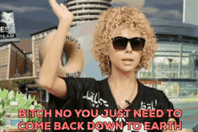 a woman with curly hair wearing sunglasses and a black shirt that says nuts on it