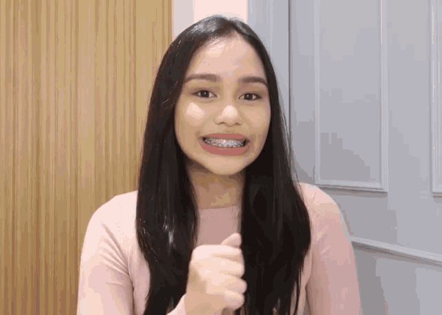 a woman with braces on her teeth is wearing a pink shirt and giving a thumbs up