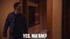 a man in a black jacket is standing in front of a door and talking to someone .