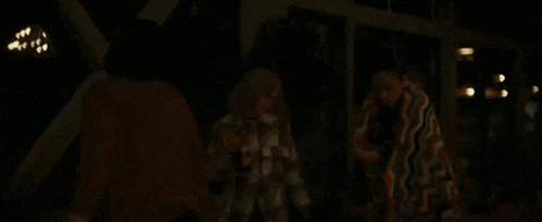 a woman in a plaid shirt is dancing with a man in a brown sweater in a dark room .
