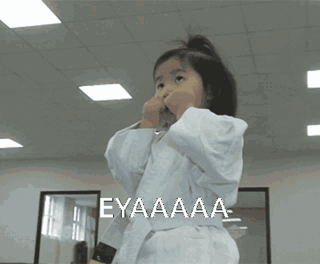 a little girl in a white karate uniform with the word eyaaa written on the bottom
