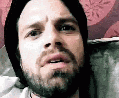 a man with a beard wearing a black hat is making a funny face .