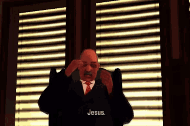 a man in a suit and tie sits in front of a window with blinds and says jesus