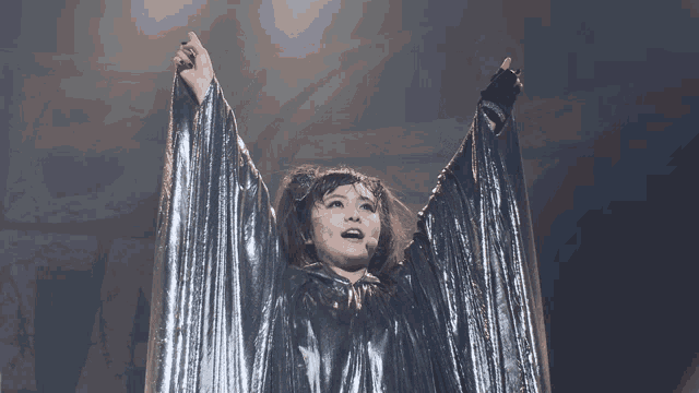 a woman wearing a silver cape with her arms outstretched