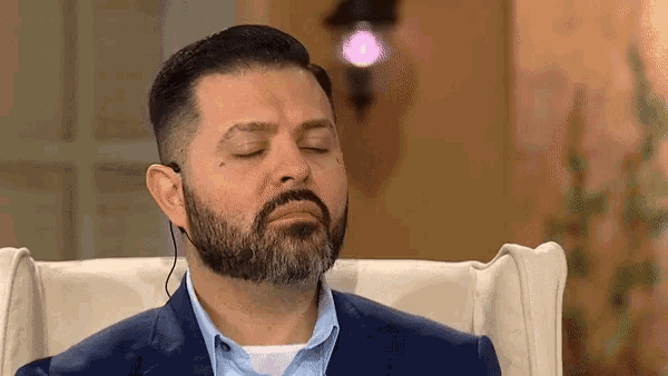 a man with a beard is sitting in a chair with his eyes closed and wearing ear buds .