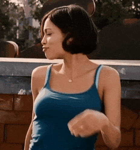 a woman in a blue tank top is dancing in front of a brick wall .