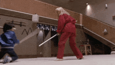 a woman in a red karate uniform is holding a stick