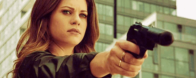 a woman is pointing a gun at the camera while standing in front of a building .
