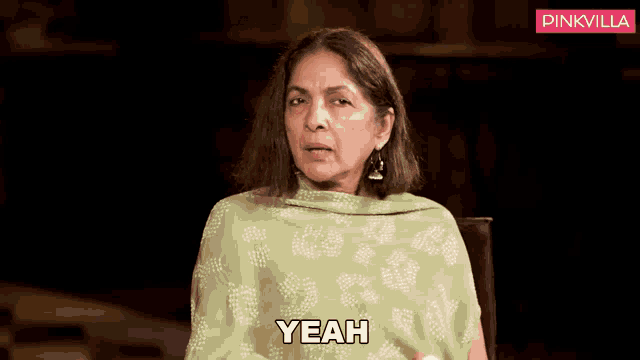 a woman in a green shawl is sitting in a chair and saying yeah
