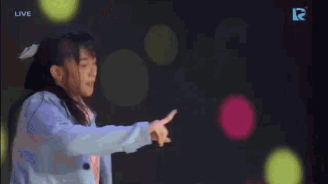 a woman in a blue jacket is dancing in front of a live r logo