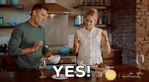 a man and a woman are sitting at a table in a kitchen and the woman is holding a glass of wine .