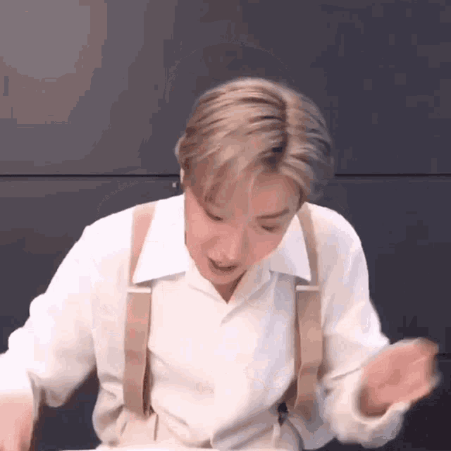 a young man wearing a white shirt and suspenders is making a funny face .