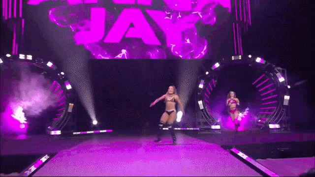 a woman in a bikini is walking down a stage with a large purple sign that says jay