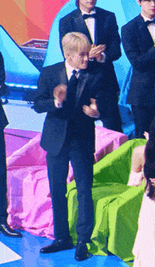 a man in a tuxedo stands in front of a green chair